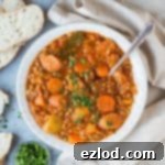 A white bowl full of vegan stew on a grey background with a cream cloth, a bowl of parsley and sliced bread.