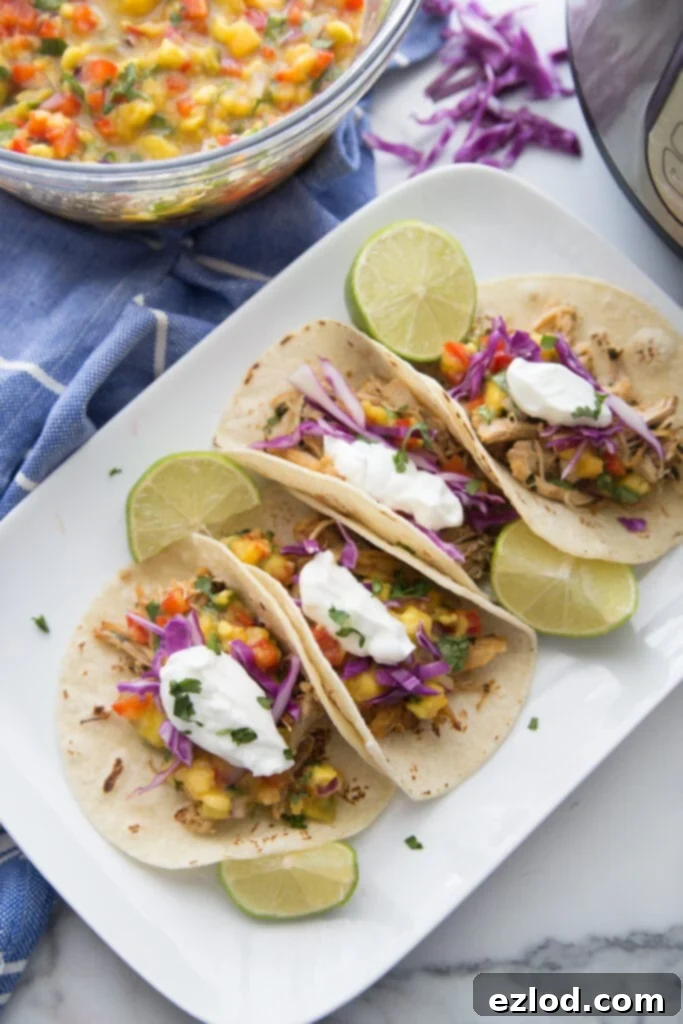 A white plate of tacos made from instant pot chicken carnitas with avocado peach salsa sitting nearby