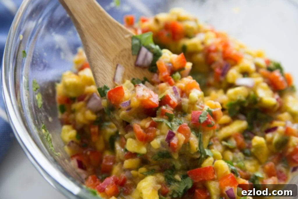 A bowl of avocado peach salsa being scooped up with a wooden spoon