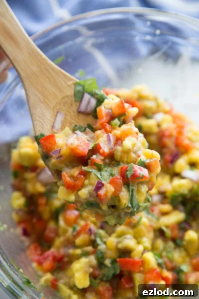 A close up of avocado peach salsa in a glass bowl on a wooden spoon. 