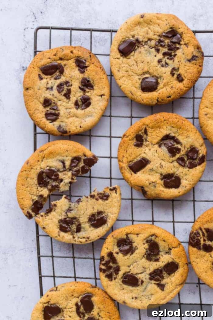 A selection of freshly baked vegan peanut butter chocolate chip cookies cooling on a wire rack, with one cookie thoughtfully broken in half to reveal its soft, chocolate-studded interior.