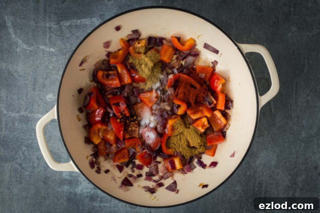 Frying a mix of chopped red onions and red bell peppers with aromatic spices in a non-stick pan, showing the rich colors and textures developing.