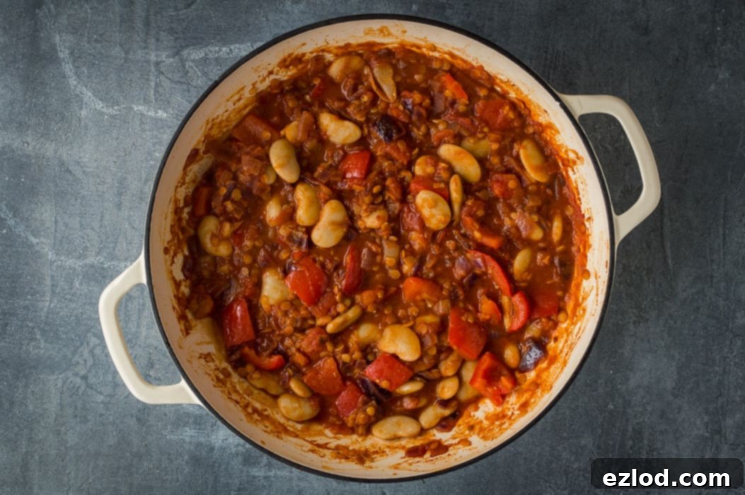 Vegan lentil and butter bean chilli simmering in a white pan, with a rich, thick sauce and visible chunks of vegetables and beans.