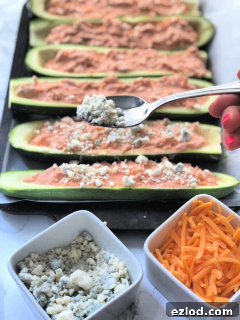 A tray of buffalo chicken stuffed zucchini being topped with blue cheese before baking