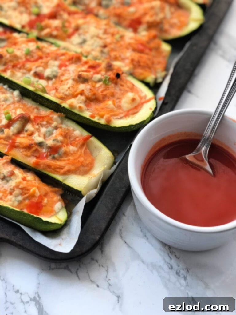 A tray of Buffalo Chicken Zucchini Boats next to a cup of hot sauce