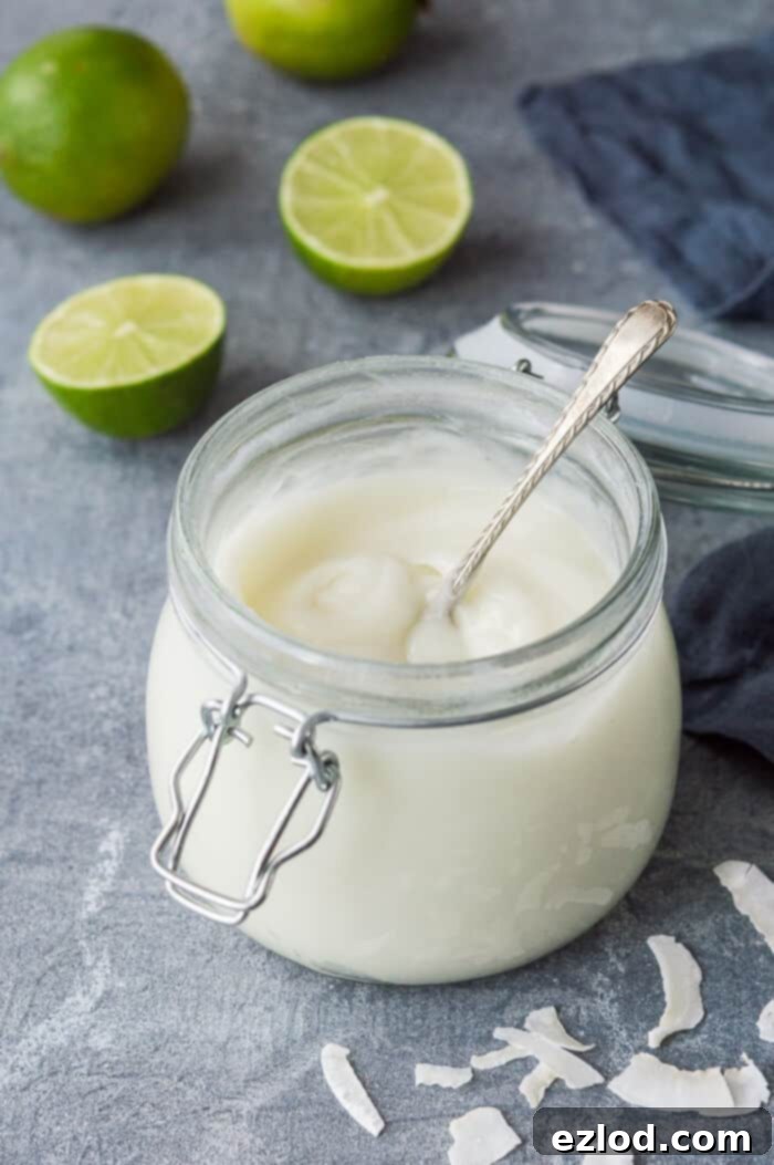 A beautifully presented clip-top glass jar brimming with smooth vegan coconut lime curd, accompanied by a spoon, set against a stylish grey background.