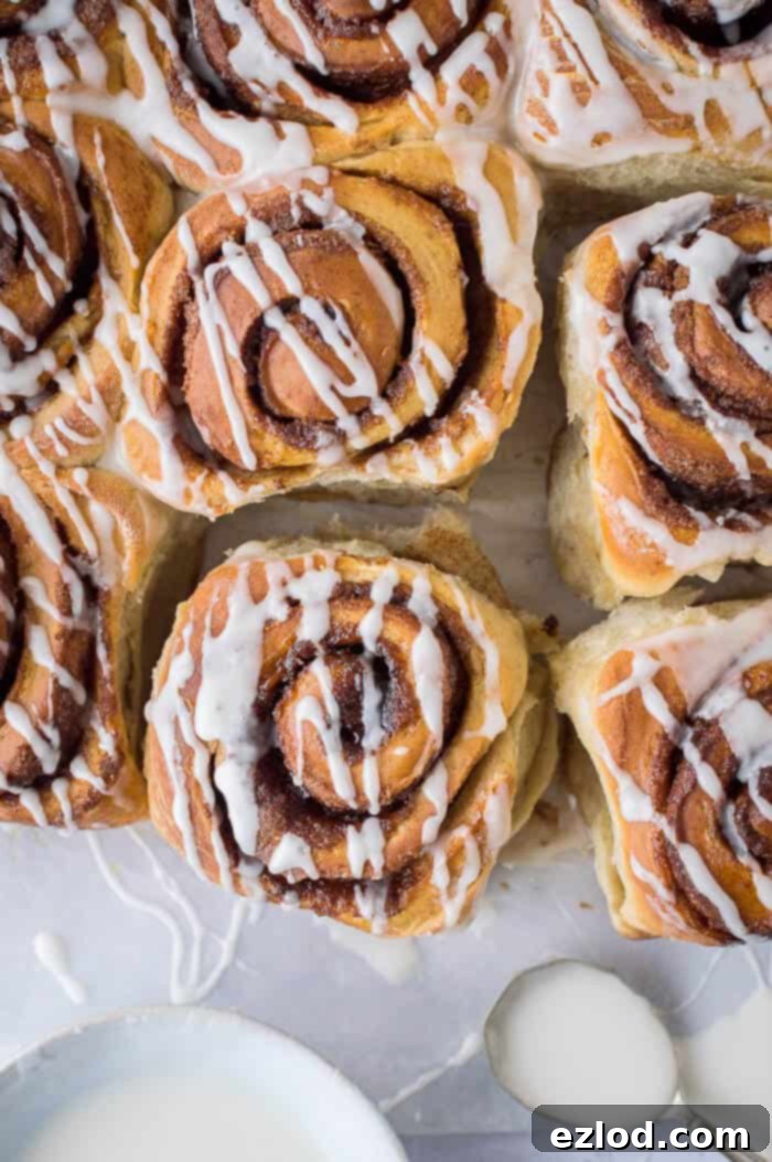 Top down shot of nine vegan banana bread cinnamon rolls with a bowl of vanilla glaze and a spoon.