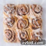 Nine vegan banana bread cinnamon rolls with vanilla glaze on a sheet of baking parchment.