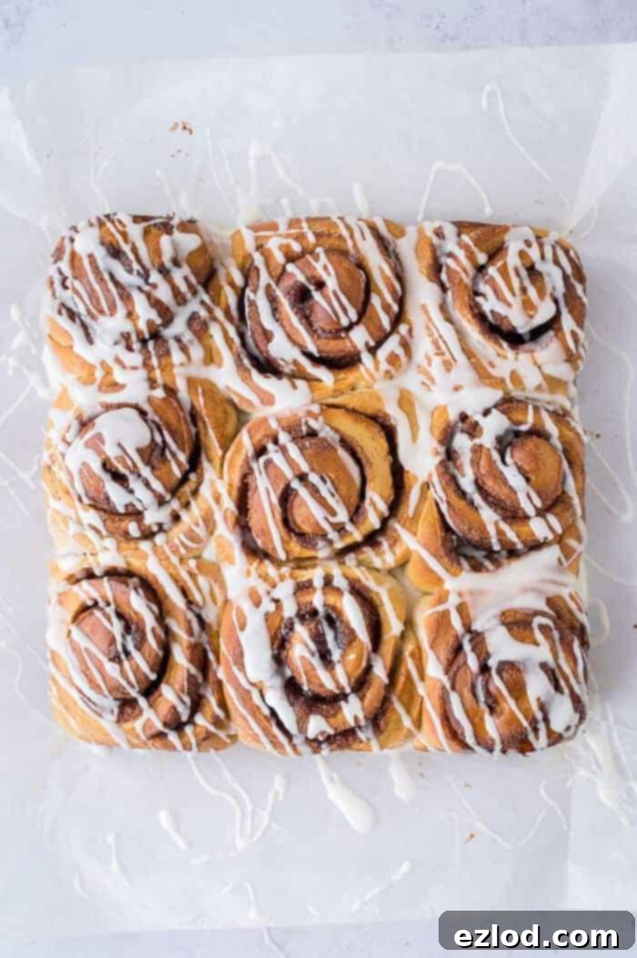 Nine vegan banana bread cinnamon rolls with a generous layer of vanilla glaze, arranged on baking parchment.