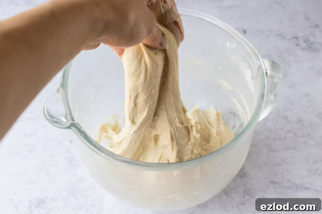 A hand stretching soft and sticky vegan banana bread cinnamon roll dough to check for elasticity.