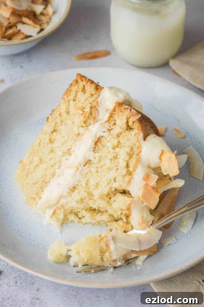 Close-up shot of a perfect slice of vegan coconut layer cake, revealing its moist texture, creamy buttercream, and vibrant lime curd layers, with a fork taking a bite.