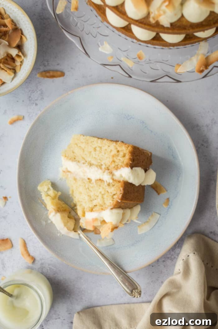 Top-down view of a single slice of vegan coconut layer cake on a grey plate against a matching grey background, highlighting the distinct layers.