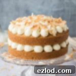 Two layer vegan coconut cake with coconut buttercream on a glass cake stand.