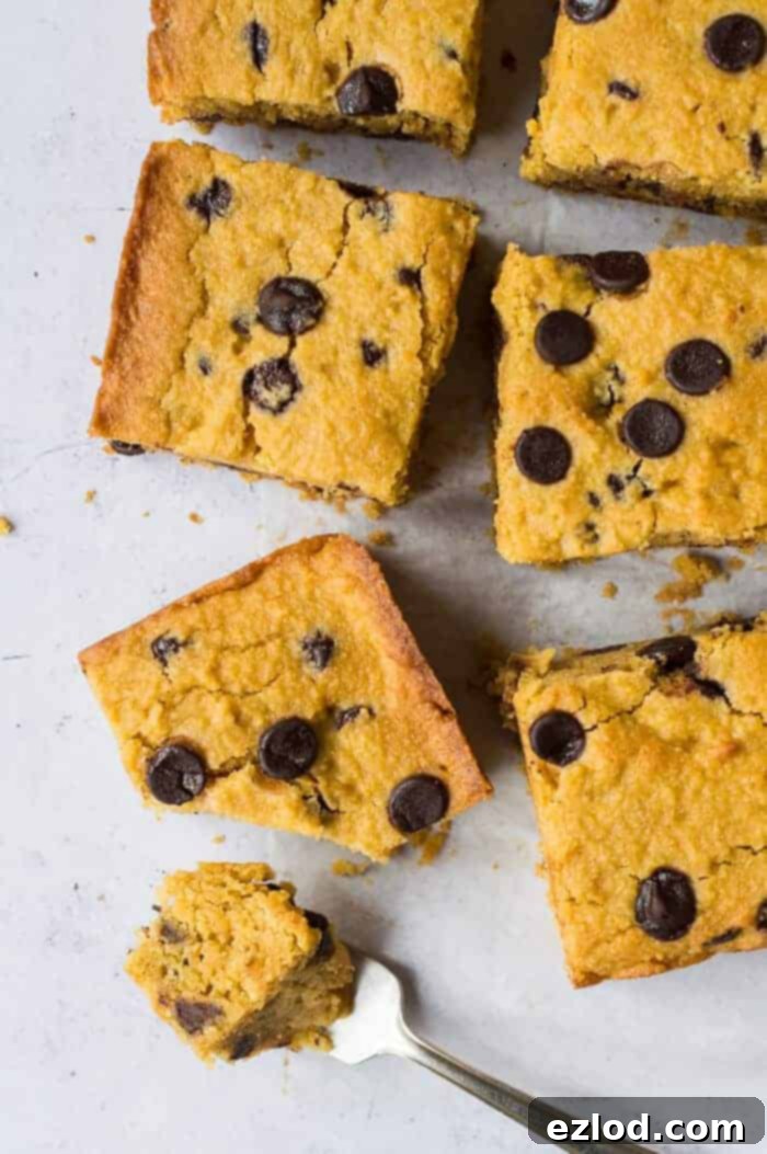 A perfectly square slice of vegan, gluten-free, low FODMAP sweet potato chocolate chip cake, sitting on a piece of baking parchment. A fork has removed a bite, revealing the cake's moist texture and generous chocolate chips.
