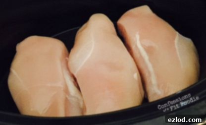 Raw boneless, skinless chicken breasts in a slow cooker pot.