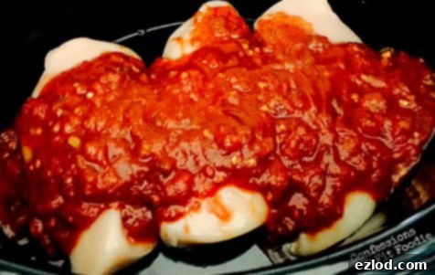 A jar of organic salsa being poured over chicken breasts in a slow cooker.