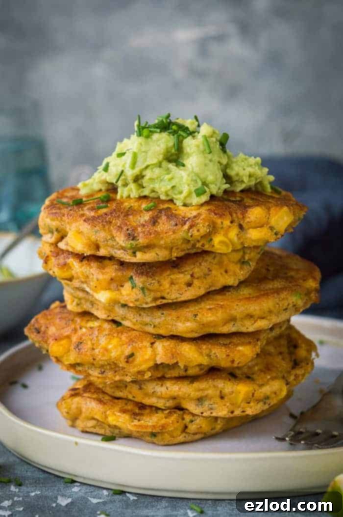 A stack of easy vegan corn fritters topped with guacamole on a white plate.