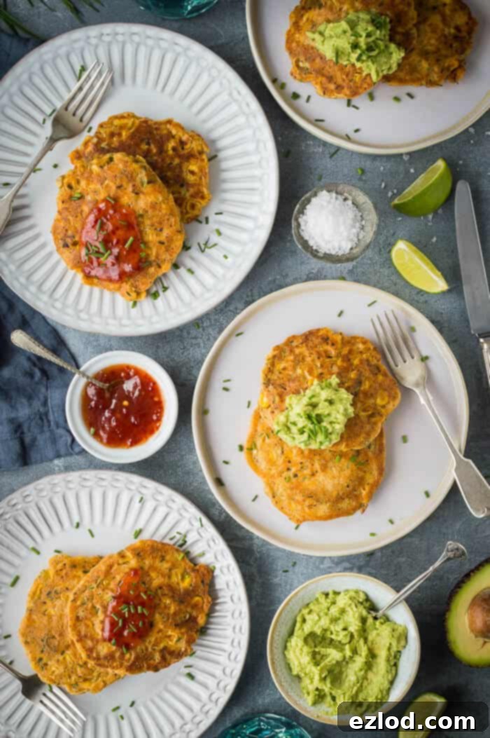 Four white plates of vegan corn fritters with guacamole and chilli sauce on a grey background.