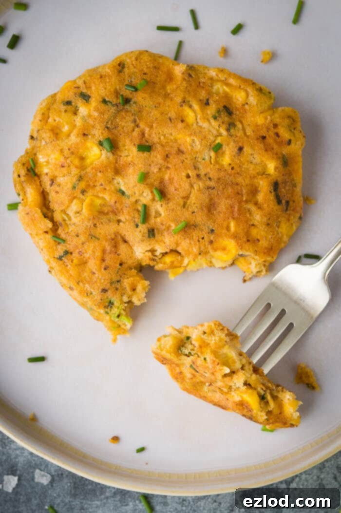 Close up of a vegan corn fritter with a forkful taken out on a white plate.