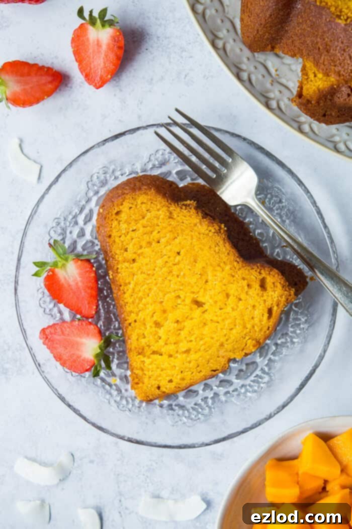 A perfect slice of vegan mango bundt cake is presented on a delicate glass plate, accompanied by a fork and vibrant sliced strawberries, ready to be savored.