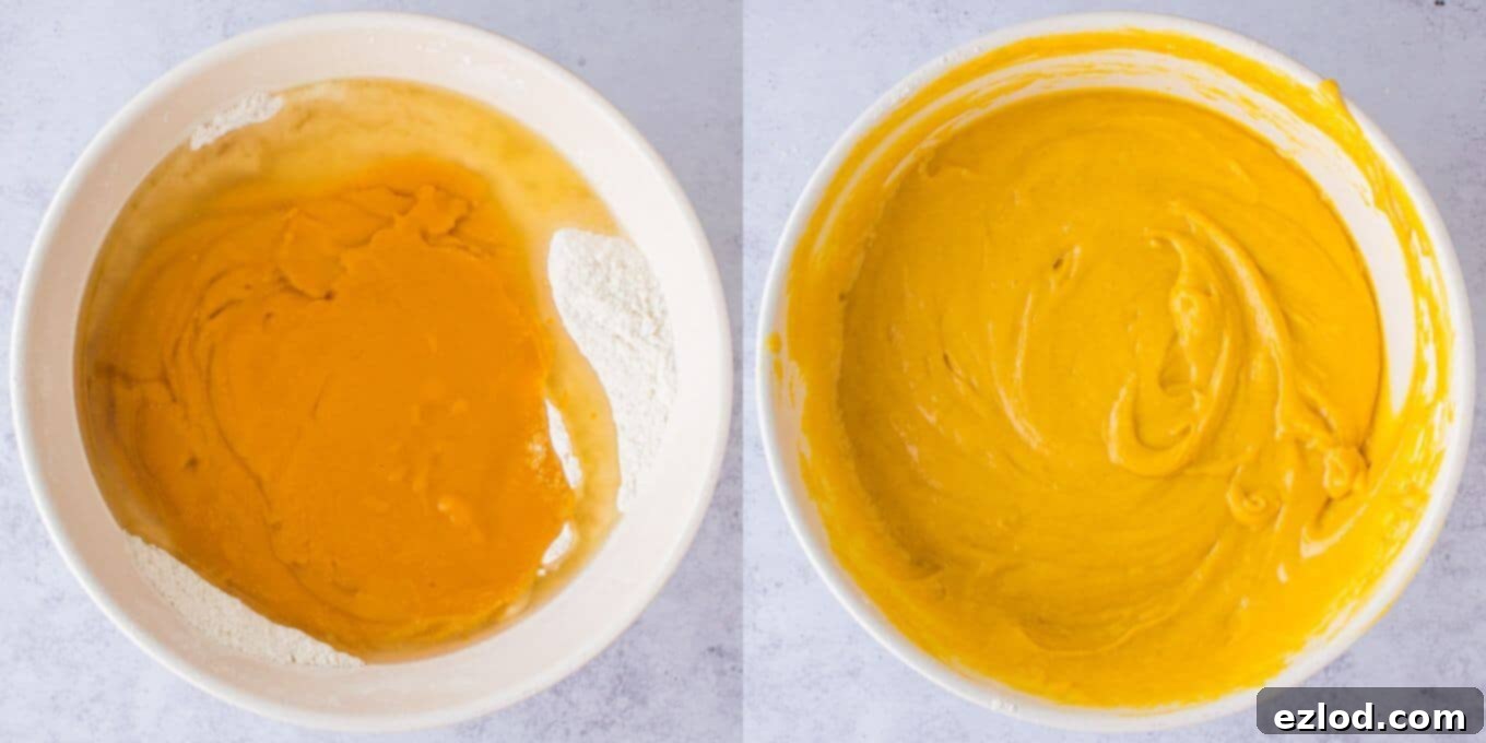 A close-up shot of cake batter being mixed in a large white bowl. The batter, a creamy yellow from mango puree, is being gently stirred by a hand holding a whisk, showing a smooth consistency without dry spots.
