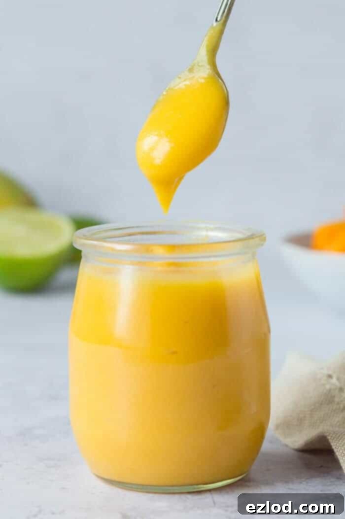 A small jar of creamy vegan mango curd with a spoonful being taken out, showcasing its smooth texture and rich yellow color.