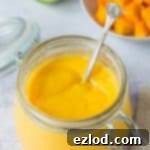 A large glass jar of eggless mango curd on a grey background, vibrant and ready to be served.