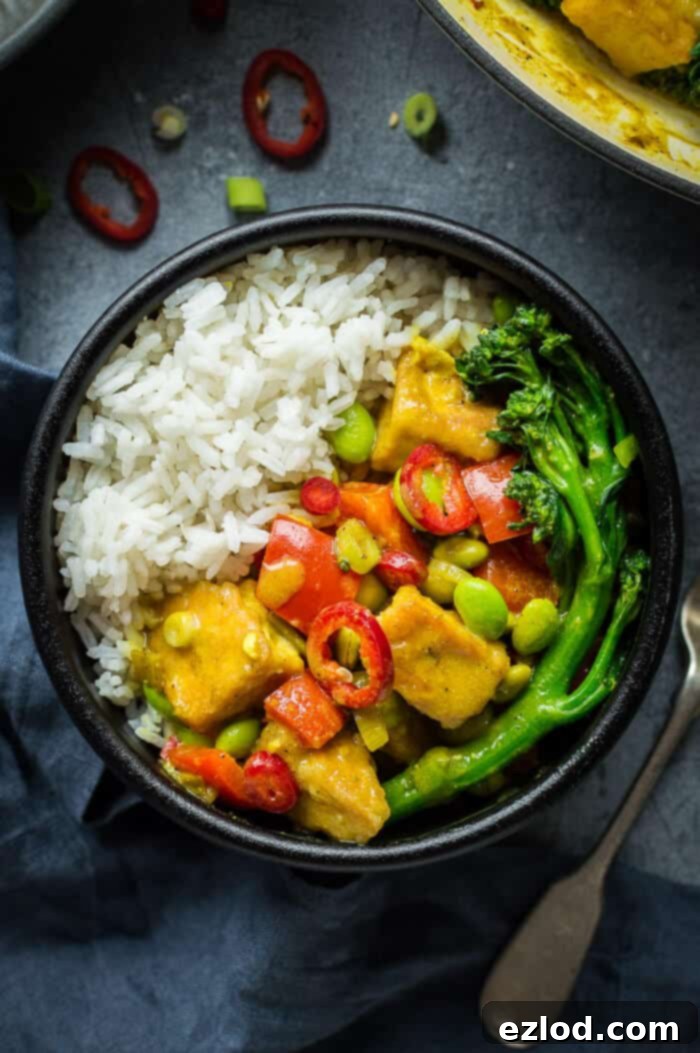 A black bowl brimming with creamy coconut lemongrass curry and fluffy white rice, artfully arranged on a minimalist grey background.