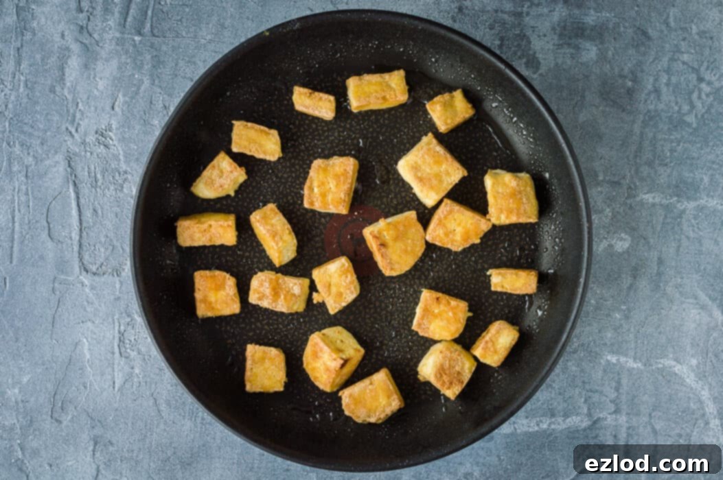Close-up shot of golden, crispy tofu cubes frying in a hot pan, demonstrating the cornflour coating's effect.
