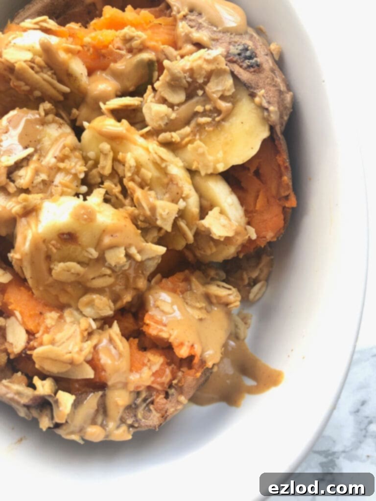 A close up shot of a sweet potato stuffed with banana, peanut butter and granola in a white bowl on a marble countertop