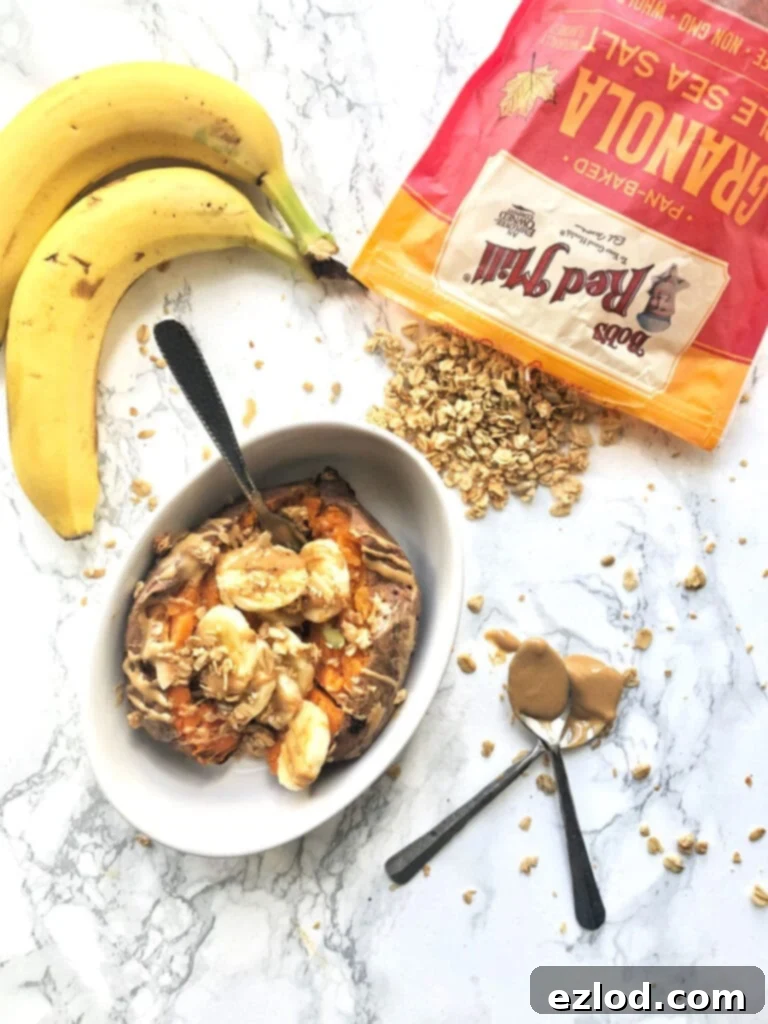 A bowl of sweet potato stuffed with banana and peanut butter on a marble counter. Bananas and a bag of Bob's Red Mill Maple Sea Salt granola are sitting on the counter nearby 