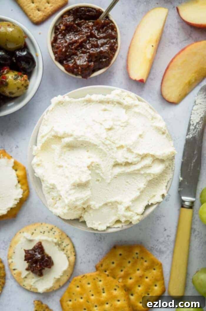 A bowl of almond feta cream cheese surrounded by crackers, apple slices, olives, a knife and a bowl of chutney