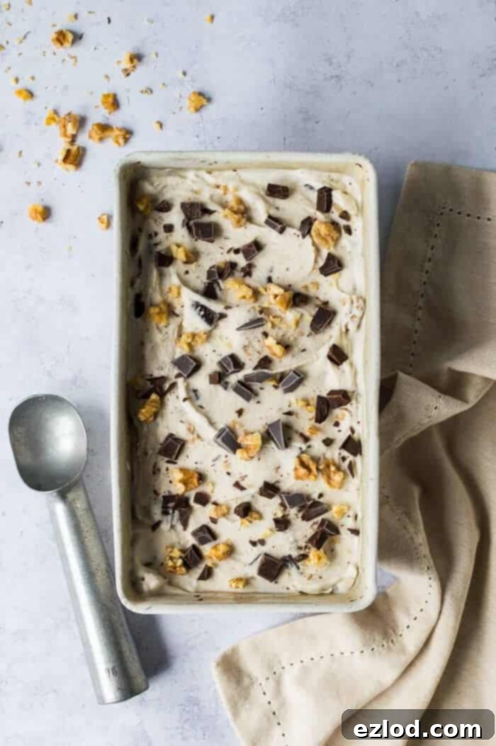 vegan chunky monkey ice cream in a loaf pan with an ice cream scoop and a beige cloth on a grey background.