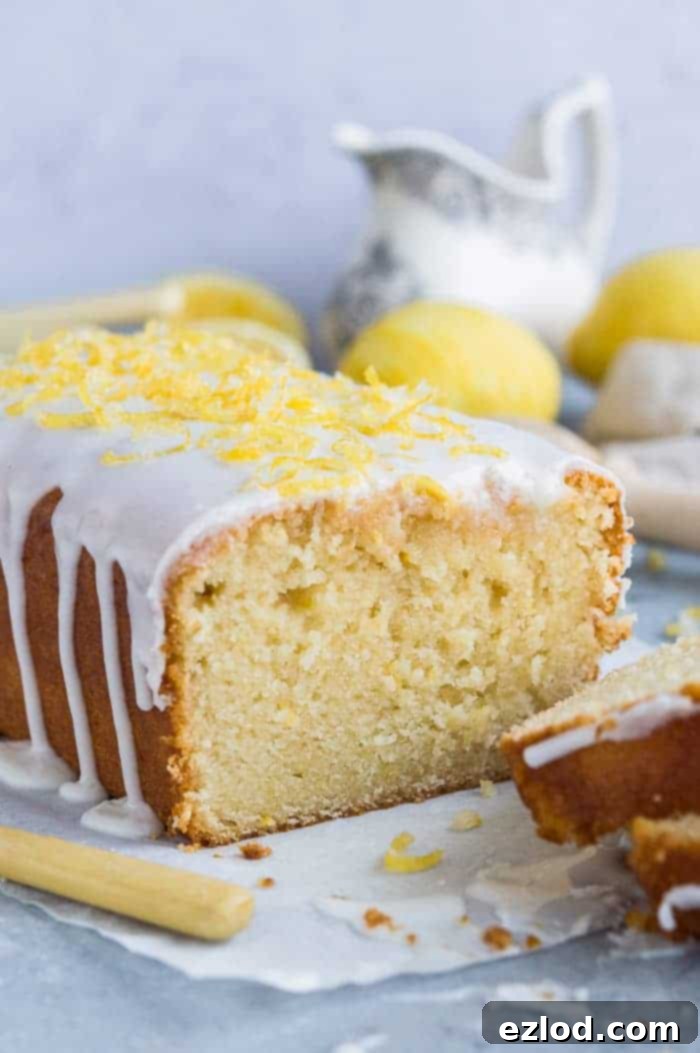 Close up of the end of a sliced vegan lemon drizzle loaf cake topped with lemon glaze and sugared lemon zest.