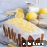 Heavenly Vegan Lemon Drizzle Cake 7 Vegan lemon drizzle cake with lemon glaze and candied lemon zest on a sheet of baking parchment with lemons and crockery in the background.