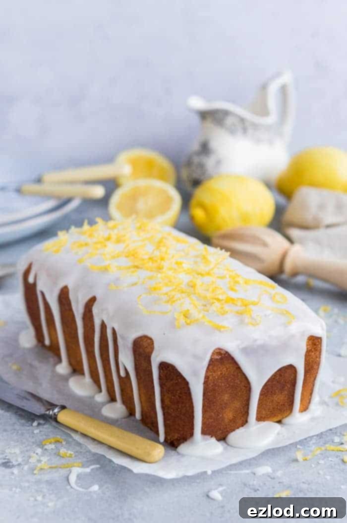 Vegan lemon drizzle cake with lemon glaze and candied lemon zest on a sheet of baking parchment with lemons and crockery in the background.