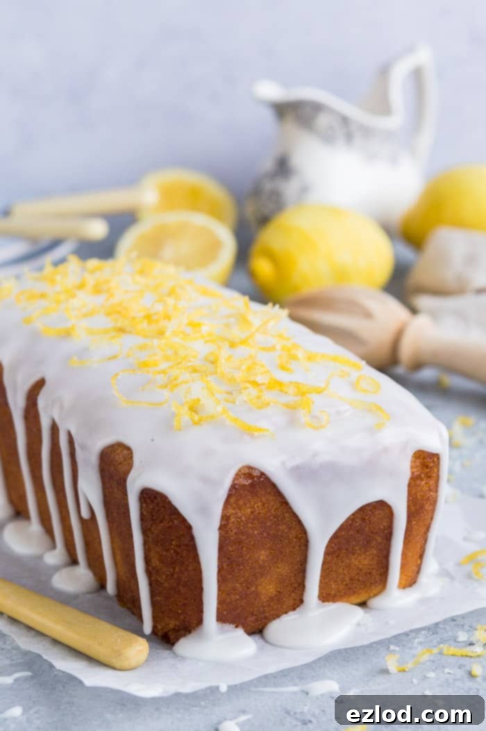 Close up of the end of an unsliced loaf of vegan lemon drizzle cake topped with lemon glaze and lemon zest.