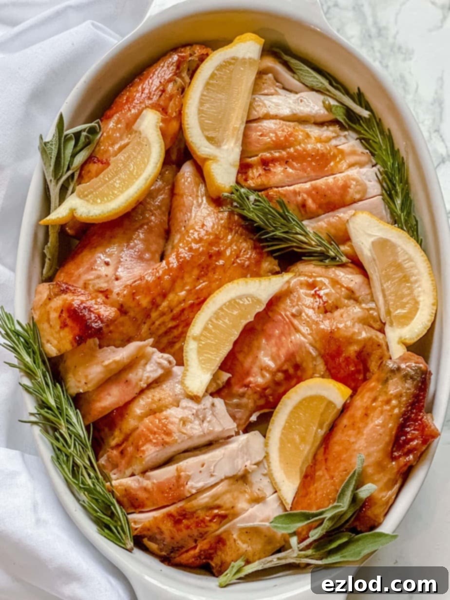 Overhead image: sliced whole oven-roasted turkey in a white baking dish with lemon slices and sprigs of rosemary for garnish.
