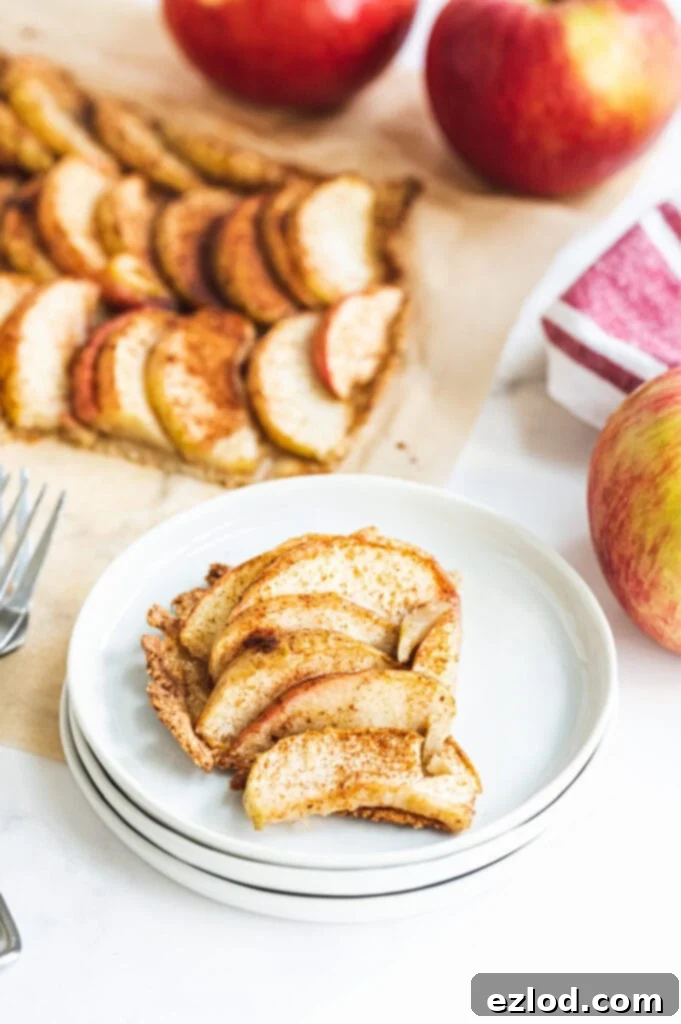 One slice of gluten-free apple tart on a stack of white plates. The rest of the tart is on a tray in the background, ready to be served.