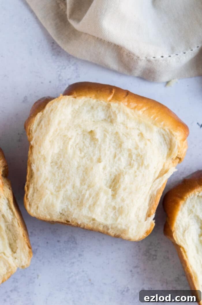 Slices of vegan Hokkaido milk bread neatly arranged on a grey background, with a soft beige cloth, highlighting their inviting texture.