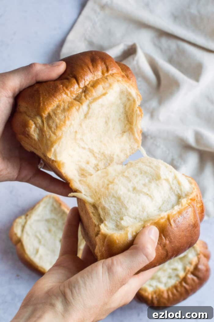 Hands pulling apart a section of a fresh vegan Hokkaido milk bread loaf, emphasizing its distinctive light and airy layers.