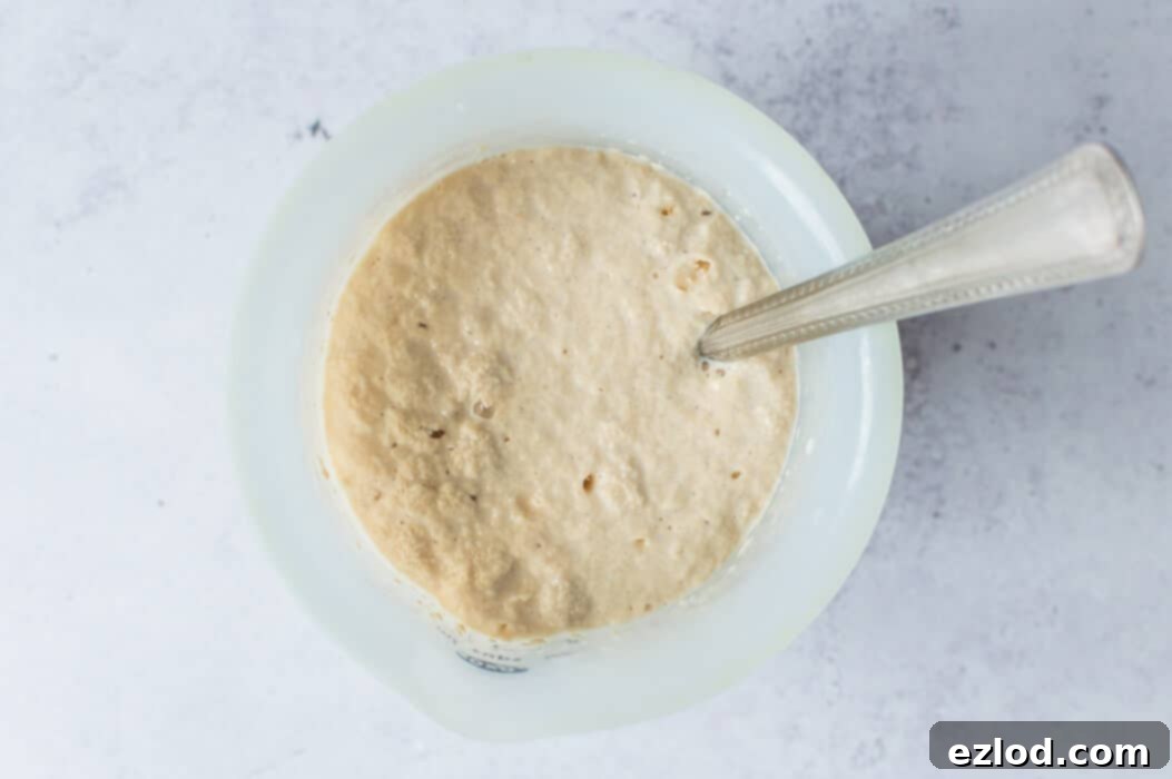 Close-up of yeast activating in lukewarm soy milk with a pinch of sugar, showing a foamy layer.