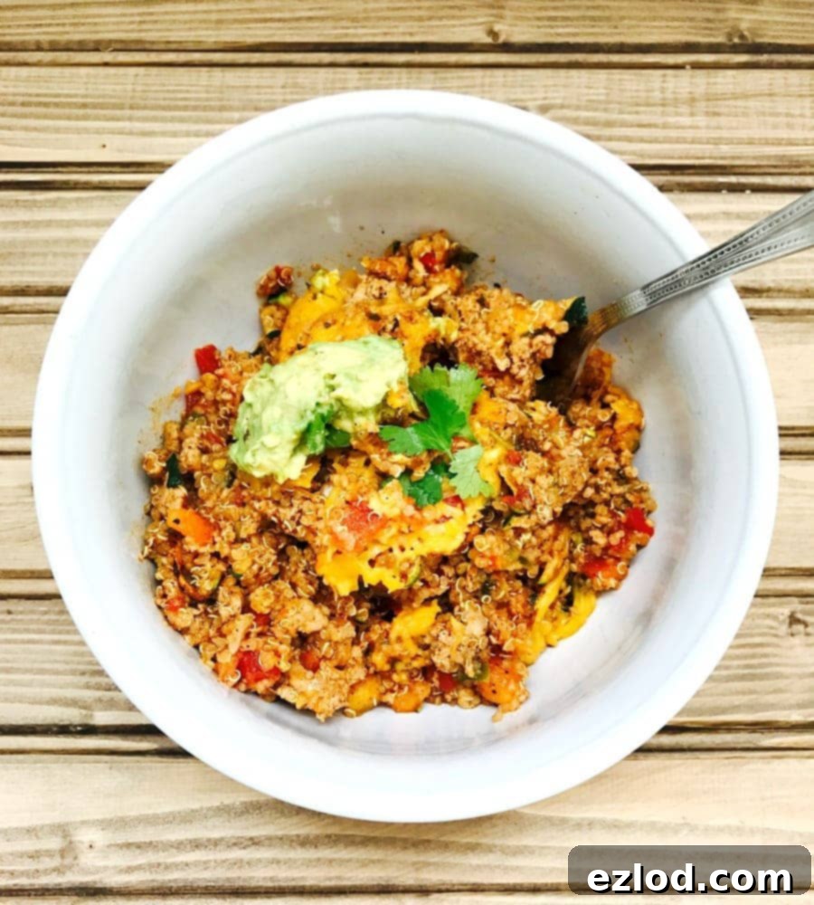 Overhead photo of Turkey Quinoa Taco Bake topped with cilantro and avocado in a white bowl with a spoon on a wooden background.