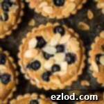 Vegan blueberry frangipane tarts on a dark baking tray.