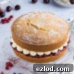 Plant-Based Victoria Sponge Delight 6 A classic vegan Victoria sponge cake, featuring two layers of vanilla sponge, generously filled with strawberry jam and piped vanilla buttercream, elegantly presented on a glass cake stand.