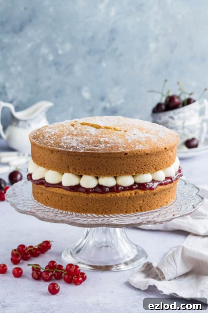 A stunning vegan Victoria sponge cake, artfully arranged on a glass cake stand, with a variety of fresh red berries, delicate crockery, and a floral backdrop, evoking a serene afternoon tea setting.