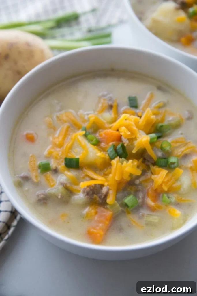 A bowl full of creamy Cheeseburger Soup topped with cheddar cheese and green onions sitting on a white table with a second bowl in the background