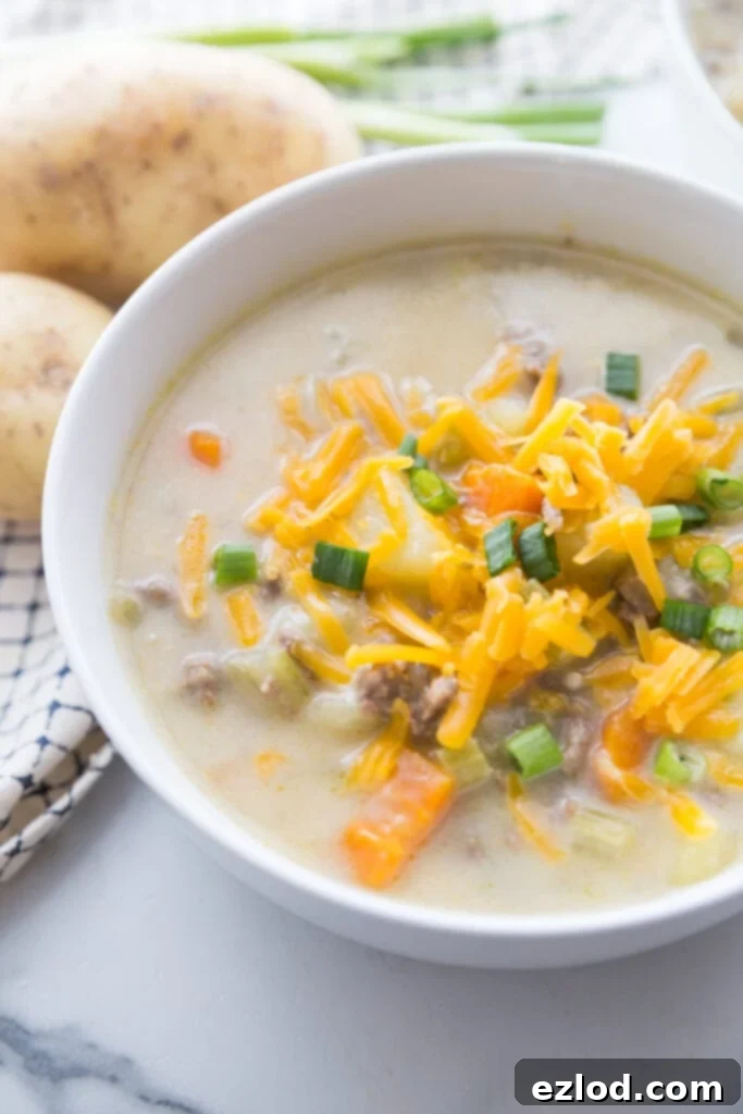  A white bowl of cheeseburger soup made in the instant pot with potatoes, carrots, celery, cauliflower, and lots of cheese