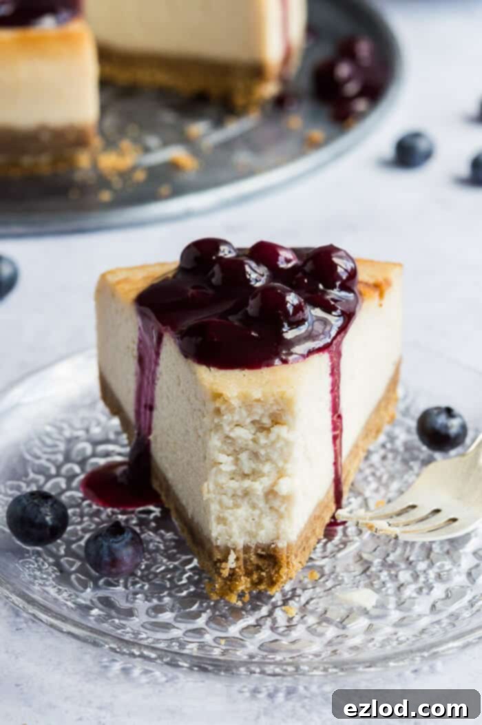 A slice of vegan lemon blueberry cheesecake on a clear glass plate, showing its creamy texture and the vibrant blueberry topping, with a fork removing a bite.