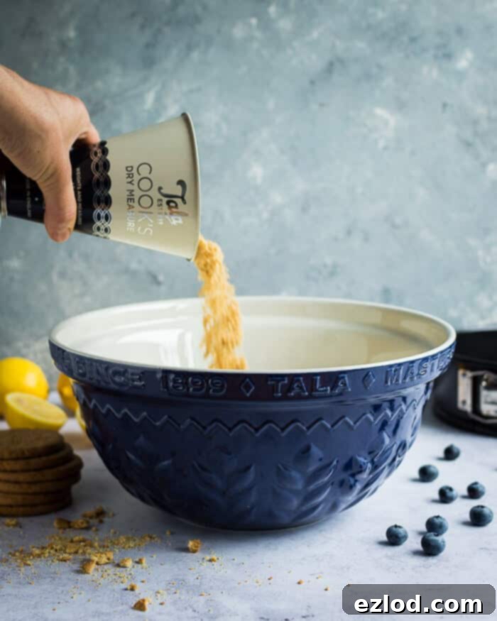 Pouring freshly crushed biscuits into a beautiful blue Tala mixing bowl, preparing for the cheesecake base.